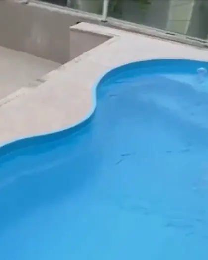 Piscina de fibra em curvas, de água azul-clara, com o deck de pedra clara em volta