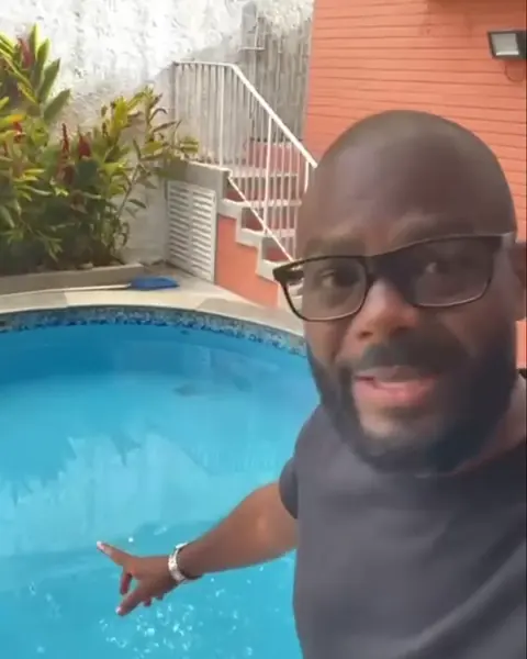 Profissional da Oliveira Piscinas apontando para uma piscina redonda de água azul, num quintal com plantas
