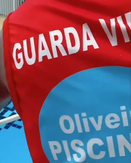 Guarda-vidas de camisa vermelha com a logo da Oliveira Piscinas, na beira da piscina